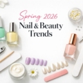 Spring 2026 nail and beauty trends flat lay with pastel nail polishes, manicure tools, floral accents, and minimalist white background styling.